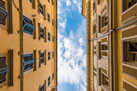 Bottom view of two typical Italian buildings and blue sky with small white clouds