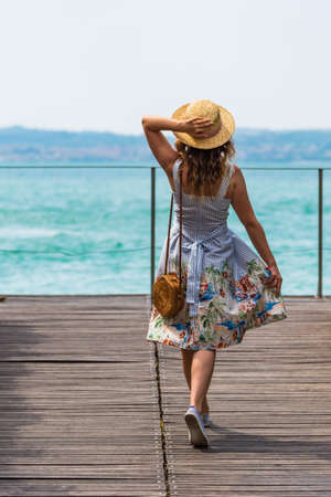 Young lady having a walk on the wooden pier facing lake Garda in Italyの写真素材
