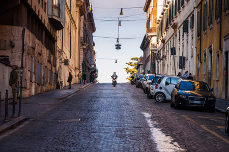 Rome, Italy - Dec 25, 2017 - Ancient romanian street in the morning and small dark scooter riding in...