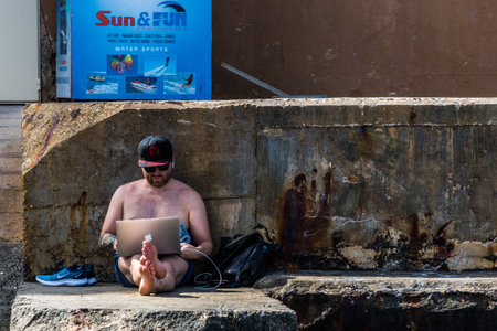 Sliema, Malta - June 24, 2019 - Developer working on his laptop on the sea shore on Maltaのeditorial素材