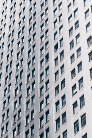A striking view of a modern high-rise building with a symmetrical facade. The photo captures the repetitive pattern of windows and the uniformity of the buildingâs design, creating a sense of depth and architectural beauty. The image is in muted tones, emphasizing the structure's sleek and contemporary style. This photograph exemplifies urban architecture and modern city life.の写真素材