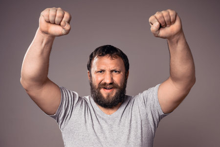 Happy handsome bearded excited man in gray t-shirt with hands up celebrating.
