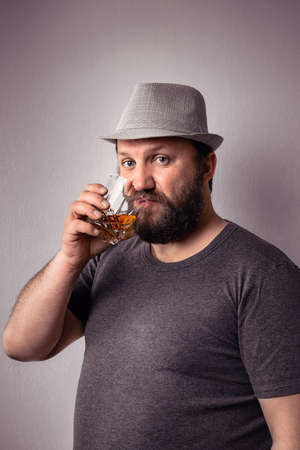 Handsome bearded man with gray t-shirt and hat drinking some strong liquor at celebration.の写真素材