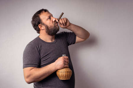 Bearded man holds a bottle of alcohol and smoking his cigar and celebrate.の写真素材