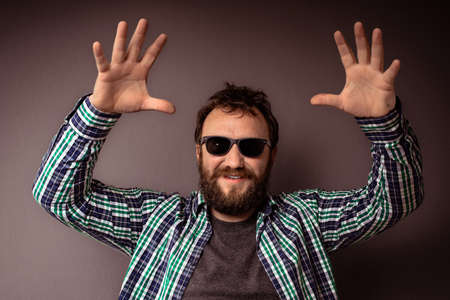 Handsome hipster bearded man with sunglasses and shirt with hands up.の写真素材