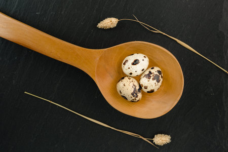 Quail eggs in wooden spoon on black stone background. Organic product.