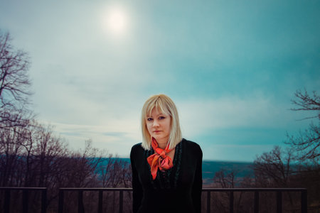 Blonde woman with red scarf and black shirt in the forest looking at the camera. Springtime, outdoor...