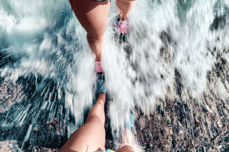 Couple standing together on the stone shore. Feet of couple covered by water wave at the seaside.の写真素材