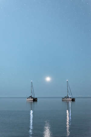 Two boats over the moonlight. Two anchored ships in the open sea under the moonlight, peninsula Kassandra, Greece.の写真素材