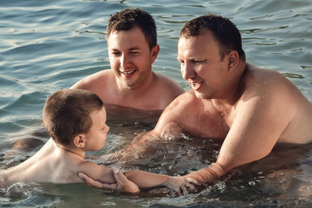 Two mans learn young boy to swim in the sea.