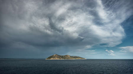 Dramatic clouds and sky over stormy sea at sunset with island on horizon.の写真素材