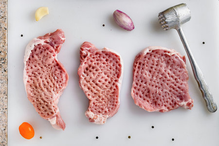 Raw meat, pork steaks on kitchen  table. Meat processing with meat hammer.