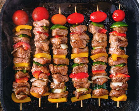 Grilled skewers on wooden sticks, pork meat and vegetables on grill.の写真素材