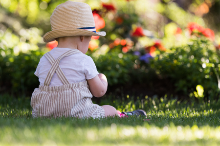 Baby boy sitting on the grass  watching flowers in the garden on beautiful spring dayの写真素材
