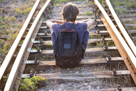 A lonely boy sitts on the railroad tracksの写真素材