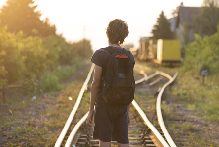A lonely boy with a bag stand on the rails at the susetの写真素材