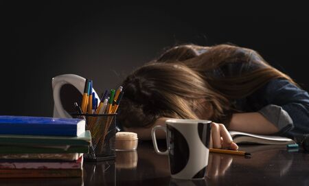 Young schoolgirl sitting at home  lying on desk filled with books training material and notebook schoolchild sleeping lazy bored to study lack of energy fatigue during learning conceptの写真素材
