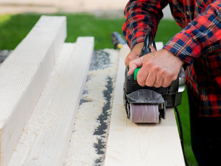 Carpenter works with belt sander in carpentry outdoor