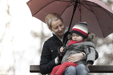 A young caucasian white mother and her baby  sitting on a bench outdoorsの写真素材
