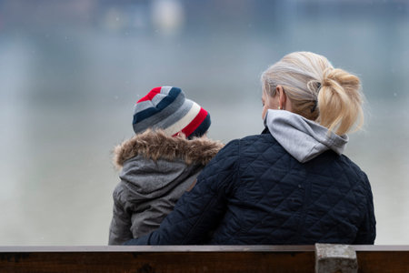 A young caucasian white mother and her baby  sitting on a bench outdoorsの写真素材