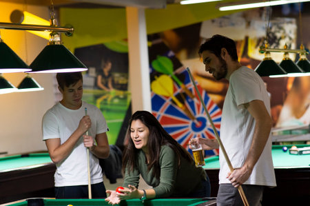 Group of young cheerful friends playing billiards