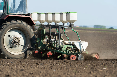Farmer with tractor seeding - sowing crops at agricultural fields in spring