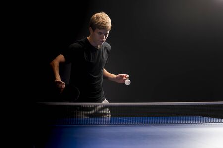 Portrait of young man playing tennis on black backgroundの写真素材