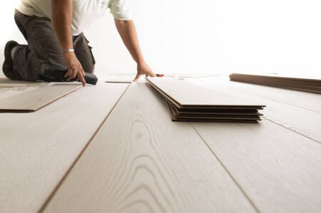 Worker making laminate flooring in apartment. Maintenance repair renovation. Wooden parquet planks indoorsの写真素材