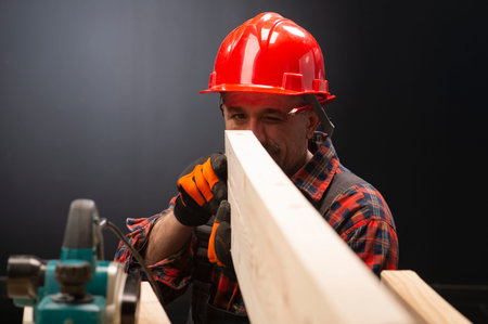 Profession, carpentry, woodwork and people concept - carpenter testing wood plank evenness at...