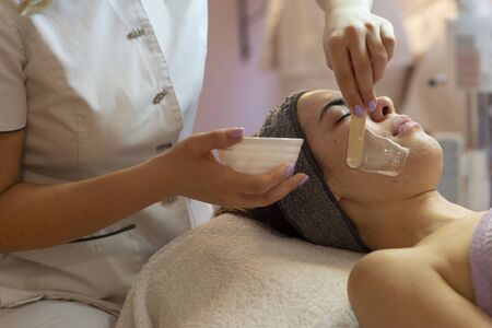 Face peeling mask, spa beauty treatment, skincare. Woman getting facial care by beautician at spa salon, side view, close-upの写真素材