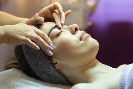 Facial massage beauty treatment. Close-up of a young womanâs face lying on back. Female patient is receiving treatment by professional therapistの写真素材