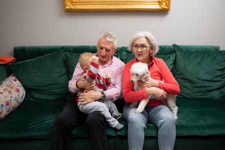 Grandparents with their young grandson and loyal poodle dog sitting together in the living roomの写真素材