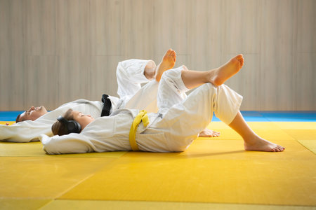 Side view of judo coach and young yellow belt judo girl  on the floor and relaxation  before...