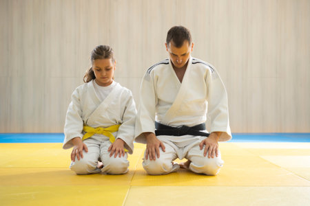Judo master and young yellow belt judo girl in white judogi kneeling
