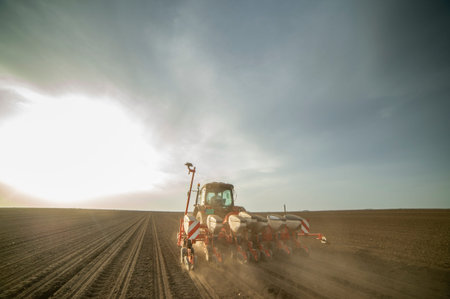 Farmer with tractor seeding - sowing crops at agricultural fields in spring