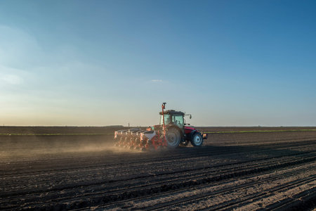 Farmer with tractor seeding - sowing crops at agricultural fields in spring