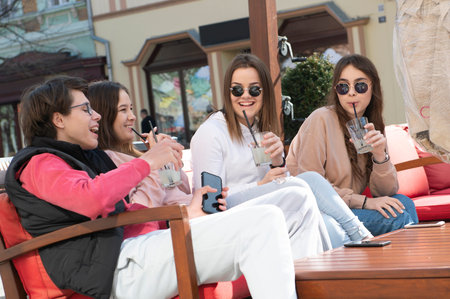 Happy friends in the garden of the cafe. Smiling young people drink lemonade at the table, laugh and...