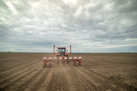 Farmer with tractor seeding - sowing crops at agricultural fields in spring