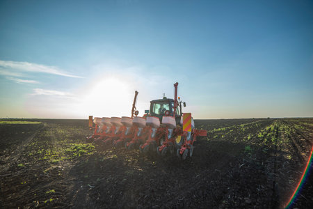 Farmer with tractor seeding - sowing crops at agricultural fields in spring