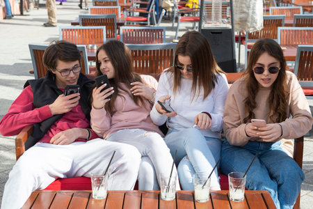 four teenagers are sitting next to each other in the garden of a cafe and having fun with their...