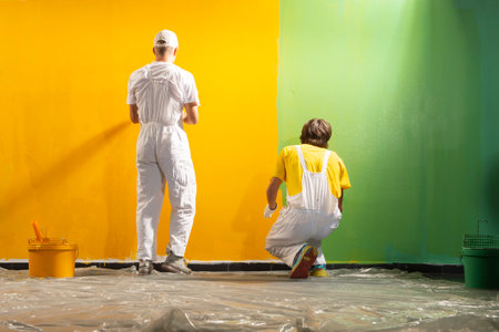 Two young decorators paint the wall yellow and greenの写真素材