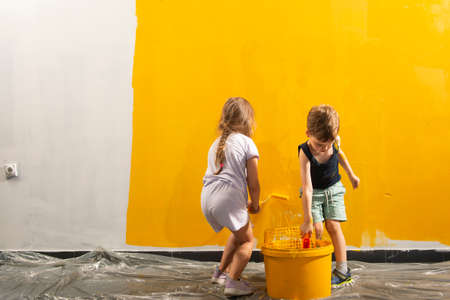 A boy and a girl with a roller, a brush and a bucket paint the wall in yellow.の写真素材