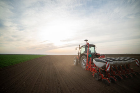 Farmer with tractor seeding - sowing crops at agricultural fields in spring