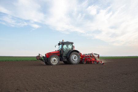 Farmer with tractor seeding - sowing crops at agricultural fields in spring