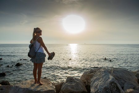 A young, beautiful woman stands by the sea at sunset - the horizon over the seaの写真素材