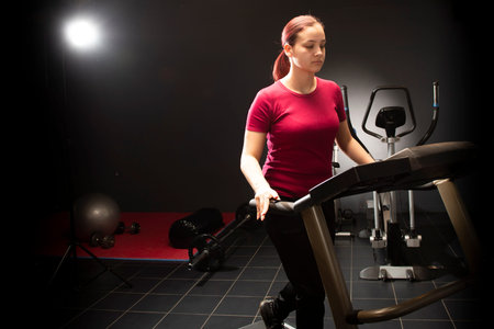 Young woman at the gym using walking treadmill on black background