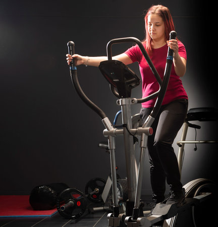 Young woman training nordic skiing in the gym on black background