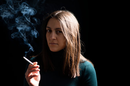 Young woman smoking cigarette on black background. Focus on cigarettesの写真素材