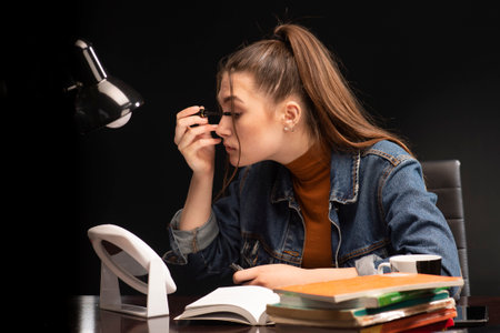 Female student, with books at the table. The girl is sitting at the table and applying makeup.の写真素材