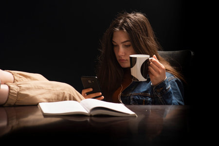 Female student sitting with her feet on a desk and a message key on a mobile phone